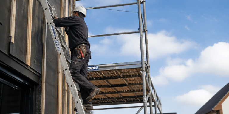 Monteur werkt op hoogte op een ladder naast een rolsteiger volgens veiligheidsregels uit de Arbowet